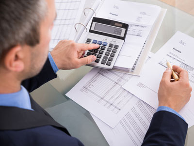 Eine Person in Anzug verwendet einen Taschenrechner, während sie auf Dokumente und Rechnungen schaut.