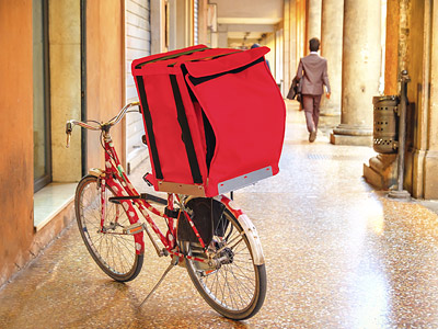 Ein rotes Lieferfahrrad mit einem großen, roten Gepäckträger steht in einer Gasse.