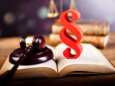 Ein Richterhammer, ein geöffnetes Gesetzbuch und das Paragraphensymbol in rot.