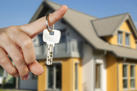 Eine Hand hält einen Schlüssel vor einem Haus.